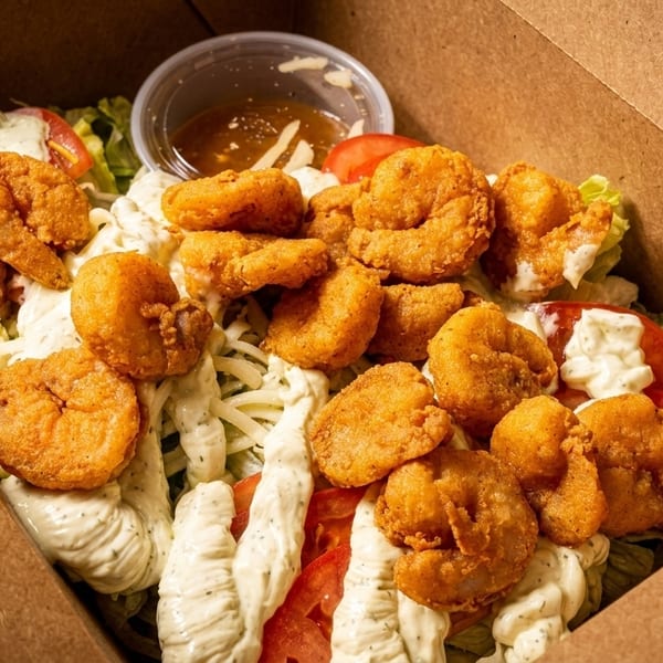 Crispy fried shrimp salad with lettuce, tomatoes, shredded cheese, and creamy dressing in a takeout box.